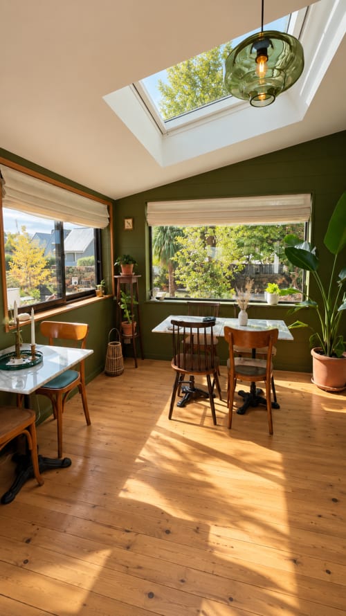 Salle à manger ensoleillée à La Maison 1903 B&B avec puits de lumière, murs verts, chaises en bois et vue sur le jardin