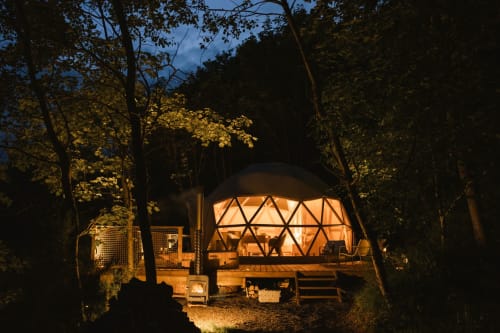 Gîte en dôme géodésique illuminé aux Cabanes du Nideck à Oberhaslach, niché parmi les arbres à la tombée de la nuit