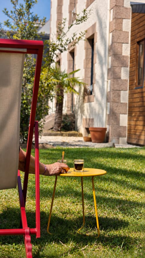 Invité se relaxant à La Maison 1903 avec un café sur table jaune dans le jardin de cour ensoleillé, Trévou-Tréguignec