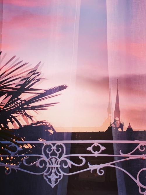 Vue du coucher de soleil illuminant la silhouette du château depuis le balcon orné de La Maison 1903 à Trévou-Tréguignec, encadré de frondes de palmier