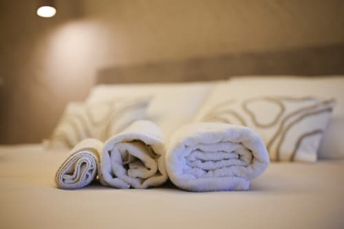 Three rolled white towels arranged on a bed at Vimini Apulian Experience hotel in Bari, with pillows and bedding visible