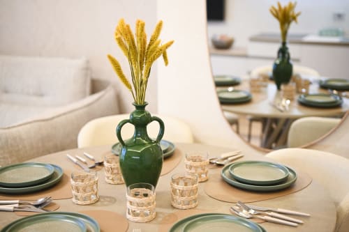 Elegant dining setup at Vimini Apulian Experience with green place settings, yellow wheat centerpiece, and sea view.