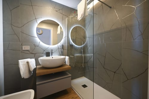 Modern bathroom in Levante apartment at Vimini Apulian Experience hotel, Bari, featuring illuminated round mirrors and stone