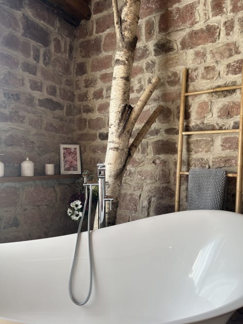 Baignoire îlot luxueuse, murs en pierre brute et décoration de branches de bouleau dans la salle de bain de la cabane Nideck