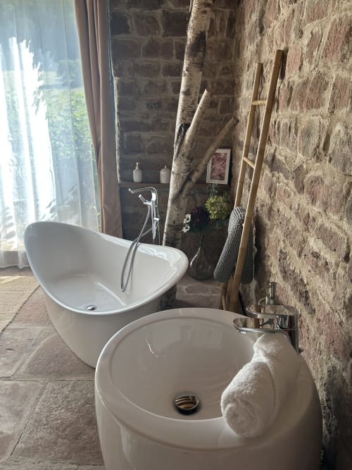 Salle de bains moderne à La Cabane de Grès avec baignoire blanche indépendante, lavabo rond, murs en pierre apparente et fenêtre