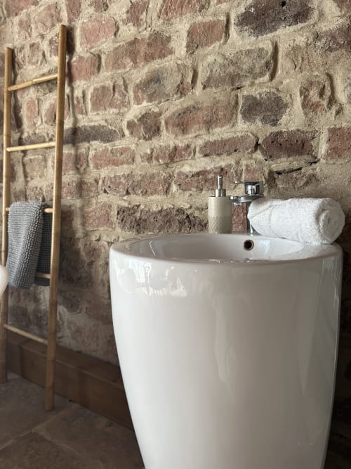 Lavabo cylindrique blanc moderne contre un mur de pierre brute rustique dans la salle de bain du gîte Les Cabanes du Nideck, Oberhaslach