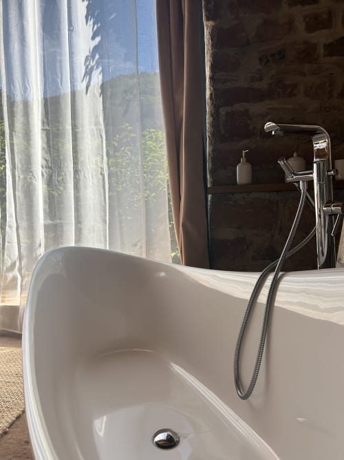 Baignoire blanche autoportante avec robinetterie chromée et vue montagne par la fenêtre du gîte Les Cabanes du Nideck