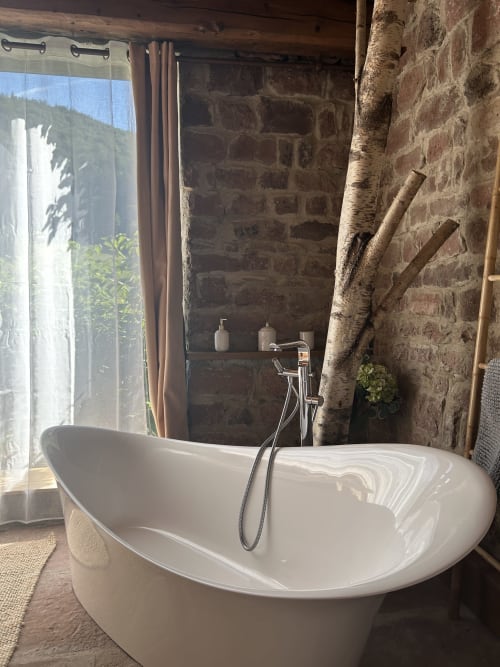 Baignoire autoportante blanche moderne dans la salle de bain rustique des Cabanes du Nideck avec vue sur les montagnes, Alsace