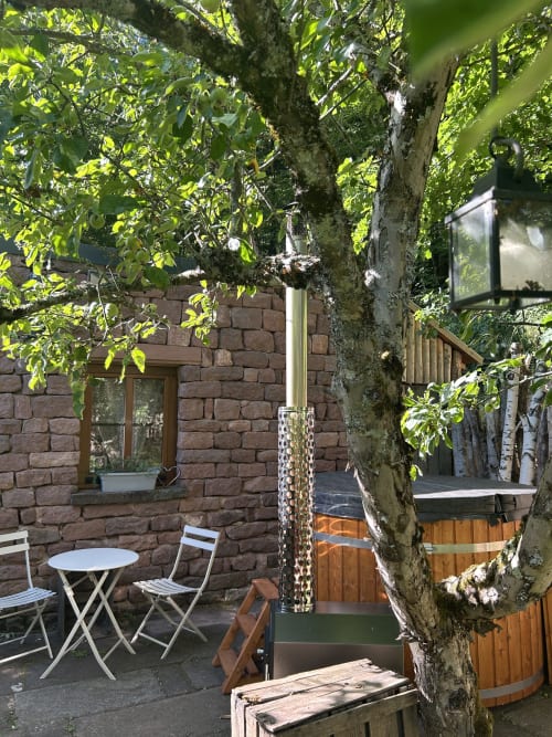 Terrasse intimiste des Cabanes du Nideck : murs en pierre, bain à remous en bois, coin bistrot, verdure luxuriante