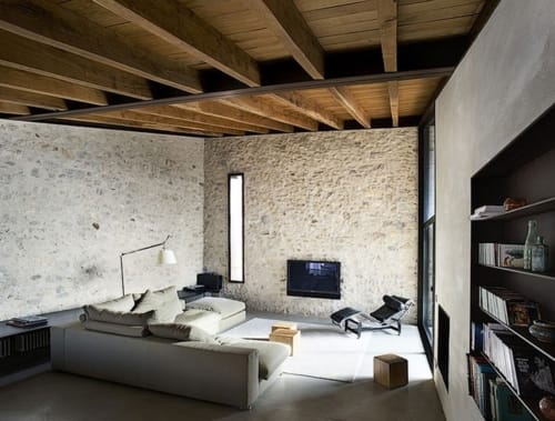 Alemanys 5 B&B modern loft with exposed stone walls, wooden beams, cream sofa, and dark shelving in Spain