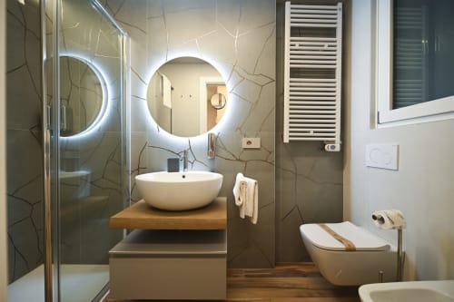 Modern bathroom in Ginestra apartment at Vimini Apulian Experience, Bari, with round lit mirror, vessel sink, and marble tile