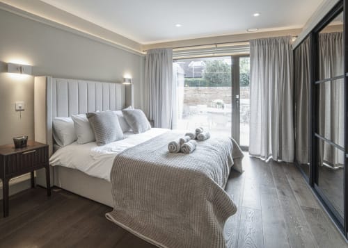 Luxurious modern bedroom at The Coach House with garden views, white upholstered bed, gray furnishings, and patio doors