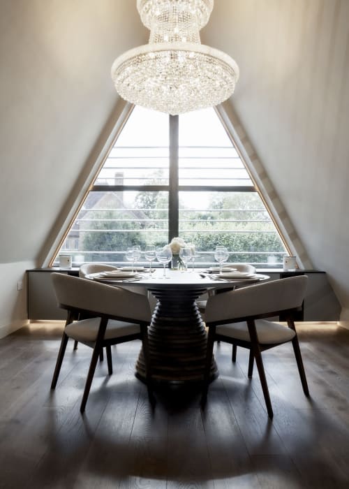 Elegant dining area at The Coach House with crystal chandelier, black pedestal table, beige chairs, and triangular window