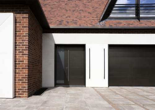 Modern villa entrance at The Coach House, featuring black door, white walls, brick chimney and paved courtyard garden view