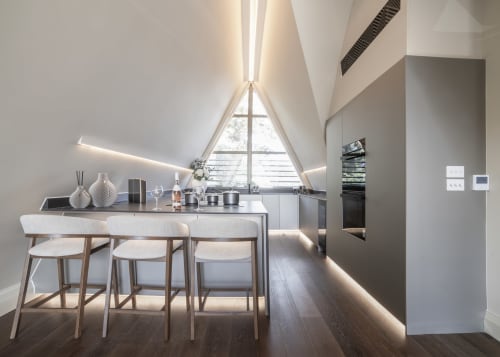 Modern attic kitchen with triangular window, dining area, stainless steel appliances, and garden views at The Coach House