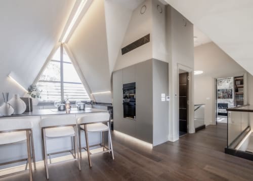 Modern attic villa kitchen with white cabinetry, dining area, and triangular windows overlooking the garden at The Coach