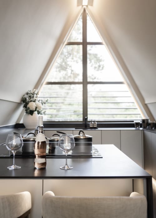 Elegant dining area with triangular window overlooking garden at The Coach House villa, featuring black table and wine