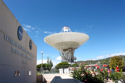 NASA Deep Space Network antenna at Las Casitas de Noe in Layos, Spain, with blooming red roses and clear blue sky
