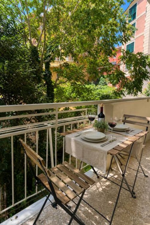 Balcone dell'appartamento di Genova con tavolo da pranzo, vino e vista sul rigoglioso giardino de La Superba Stay