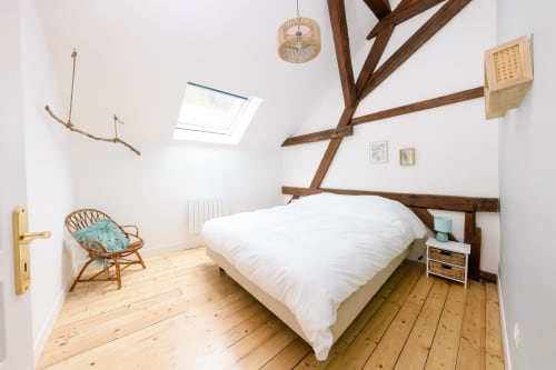 Chambre rustique aux poutres apparentes, literie blanche, puits de lumière et fauteuil en osier aux Cabanes du Nideck