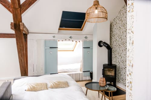 Chambre de mezzanine douillette aux Cabanes du Nideck avec poutres apparentes, poêle à bois, suspension en osier et fenêtres de toit