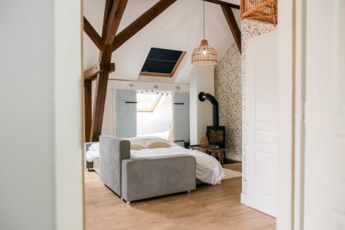 Chambre cosy aux Cabanes du Nideck avec poutres apparentes, lit gris capitonné et lucarne à Oberhaslach