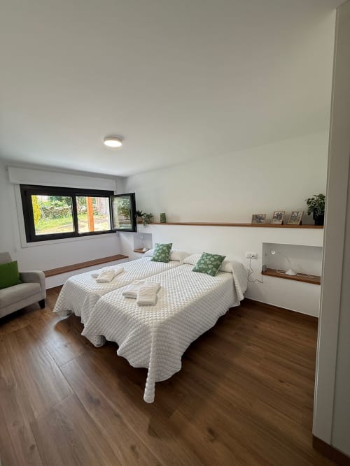 Luminoso dormitorio del hotel Bikarte en Sober con camas gemelas, suelos de madera y vistas al jardín a través de ventanas con marco negro