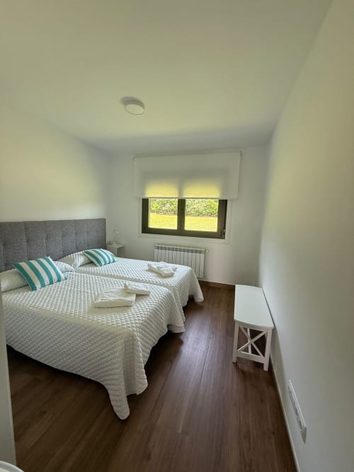 Luminoso dormitorio del hotel Bikarte en Sober con dos camas, almohadas a rayas, suelo de madera y ventana con vistas al verde