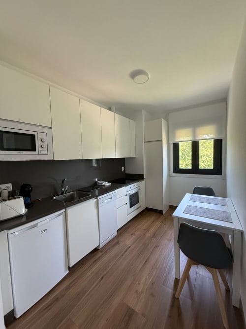 Cocina moderna en la habitación Bikarte Castiñeiros de Sober con muebles blancos, encimera negra, mesa de comedor y grandes ventanales