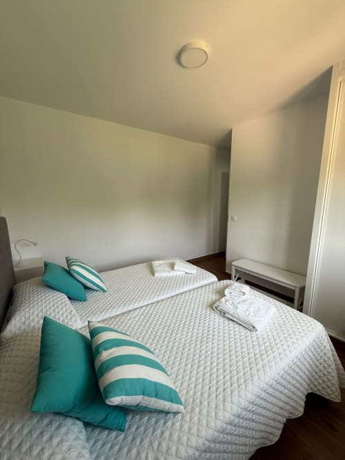 Luminosa habitación del hotel Bikarte en Sóbor con dos camas, almohadas color turquesa, ropa de cama blanca y luminaria de techo