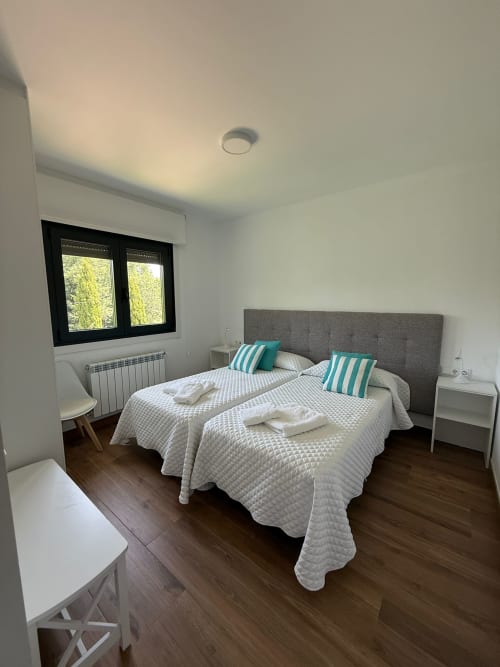 Dormitorio moderno en Bikarte Castiñeiros de Sober con camas gemelas, cabecero gris, almohadas turquesas y suelo de madera