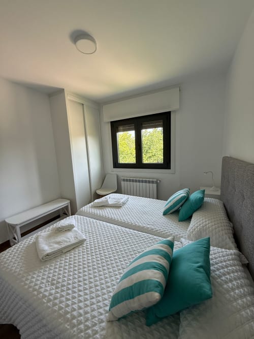 Habitación doble en el hotel Bikarte de Sober con dos camas, almohadas verde azulado, ventana con marco negro, radiador y lámpara de techo