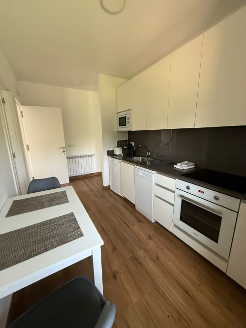 Cocina moderna del hotel Bikarte en Sober con muebles color crema, encimera negra, mesa de comedor y suelos de madera