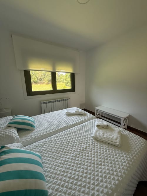 Dormitorio luminoso del hotel Bikarte en Sober con dos camas, almohadas a rayas y vistas al campo a través de dos ventanas