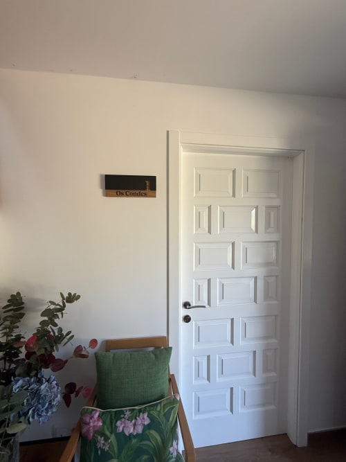 Entrada de habitación del hotel Bikarte en Sober con puerta blanca, silla verde, flores y placa Os Condes