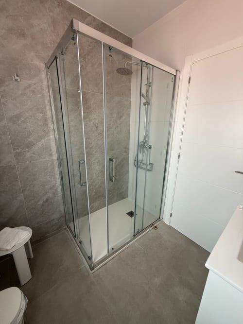 Baño moderno del hotel Bikarte en Sober con cabina de ducha de cristal, lavabo blanco y pisos de azulejos grises