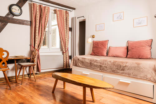 Chambre studio douillette aux Gîtes d'Avalon, Ribeauvillé, avec lit de repos, coussins corail et mobilier rustique en bois