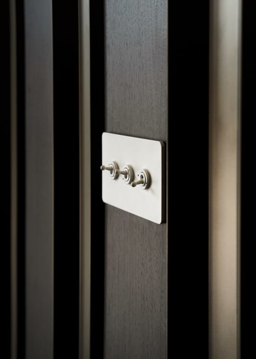 Triple toggle light switch with white plate on dark wood paneling at The Coach House hotel, Oxford