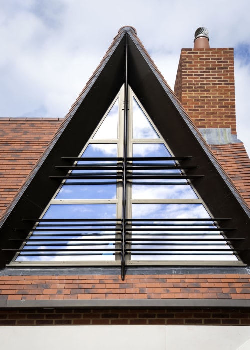 Triangular attic window with horizontal blinds on brick building at The Coach House, Oxford