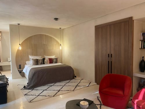 Chambre suite Jardin Sakina à Marrakech avec lit king-size, tête de lit cintrée, luminaires suspendus, fauteuil rouge