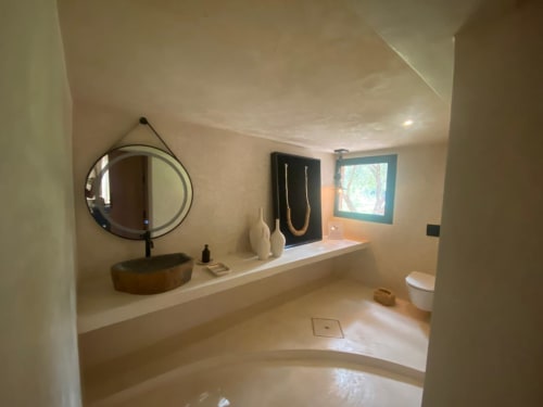Salle de bains moderne du Jardin Sakina Marrakech avec miroir rond, vasque en pierre, fenêtre bleue et douche spacieuse