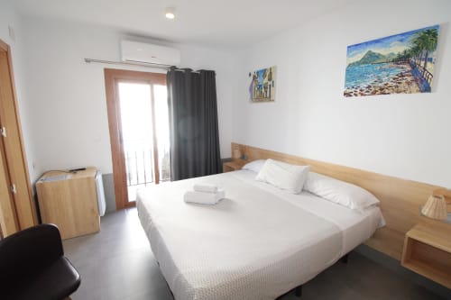 Espaciosa habitación doble en Hostal Fornet Altea con cama de madera, aire acondicionado y obras de arte costero en paredes blancas