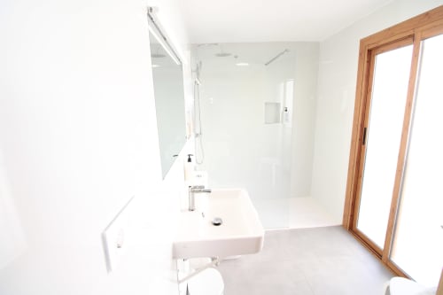 Baño moderno con lavabo blanco, inodoro, amplia ducha con mampara de cristal y puerta de madera en Hostal Fornet Altea
