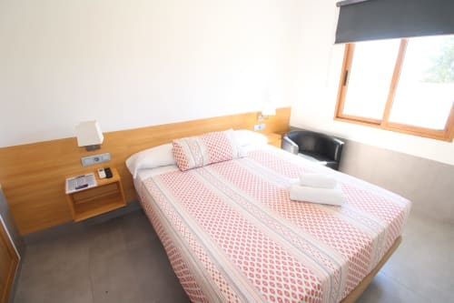 Luminosa habitación doble en Hostal Fornet Altea con ropa de cama roja estampada, cabecero de madera y vistas a la montaña