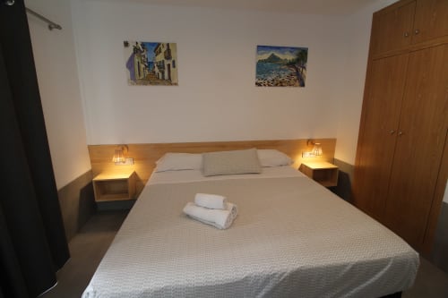 Cómoda habitación doble en Hostal Fornet Altea con mesitas de noche de madera, iluminación cálida y cuadros con vistas de montaña