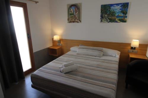 Dormitorio moderno en Hostal Fornet Altea con cama doble, cabecero de madera, lámparas gemelas y cuadros costeros en paredes blancas