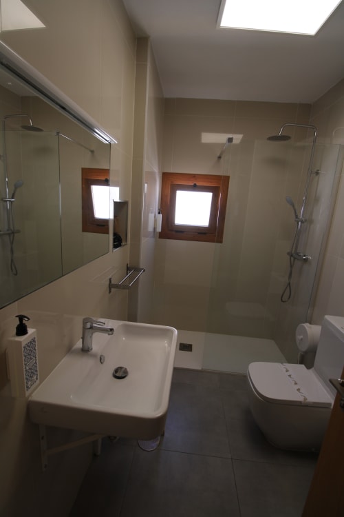 Baño moderno en Hostal Fornet Altea con ducha doble, lavabo, inodoro y ventanas de claraboya en Altea, España