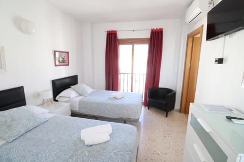 Habitación doble luminosa en Hostal Fornet Altea con dos camas, TV, aire acondicionado y balcón con vistas a la montaña y cortinas rojas