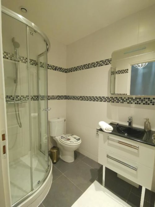 Modern bathroom in Deluxe Apartment at Hôtel OH Sèvres Autrement, featuring shower enclosure, white vanity, and mosaic tile