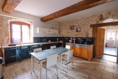 Cuisine-salle à manger en pierre avec poutres apparentes, crédence carrelage noir, meubles bois et style contemporain